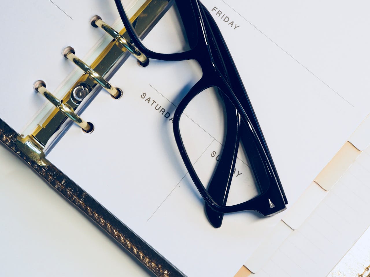 gallery-6 Close-up of eyeglasses resting on an open planner highlighting the weekend.